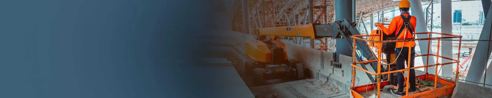 Worker in an orange safety vest standing on an elevated work platform at a construction site