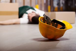 Yellow hard hat on the floor with a person lying in the background