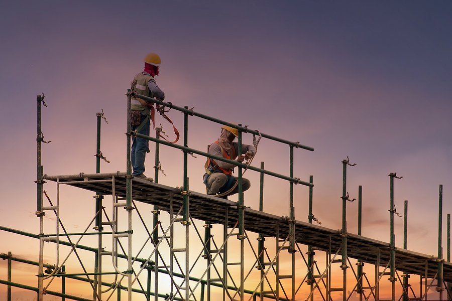 Two men atop metal construction scaffolding.