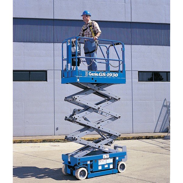 Worker operating a blue scissor lift beside a building