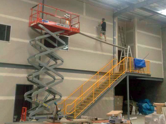 Scissor lift raised inside a building near a worker on an elevated walkway