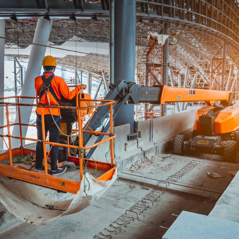 Worker on an orange boom lift platform inside a construction site